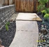 A concrete walkway leading to a wooden fence in a backyard.