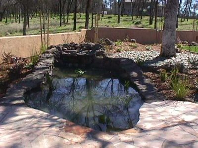 A pond surrounded by rocks and trees with a house in the background