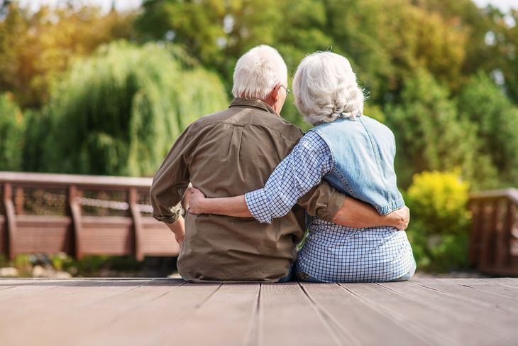 Two people sitting close together on a bench in a park, with an arm around each other.