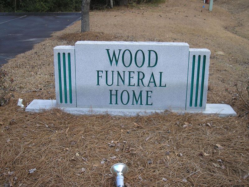 Wood Funeral Home sign in a grassy roadside area with teal stripes on a stone base
