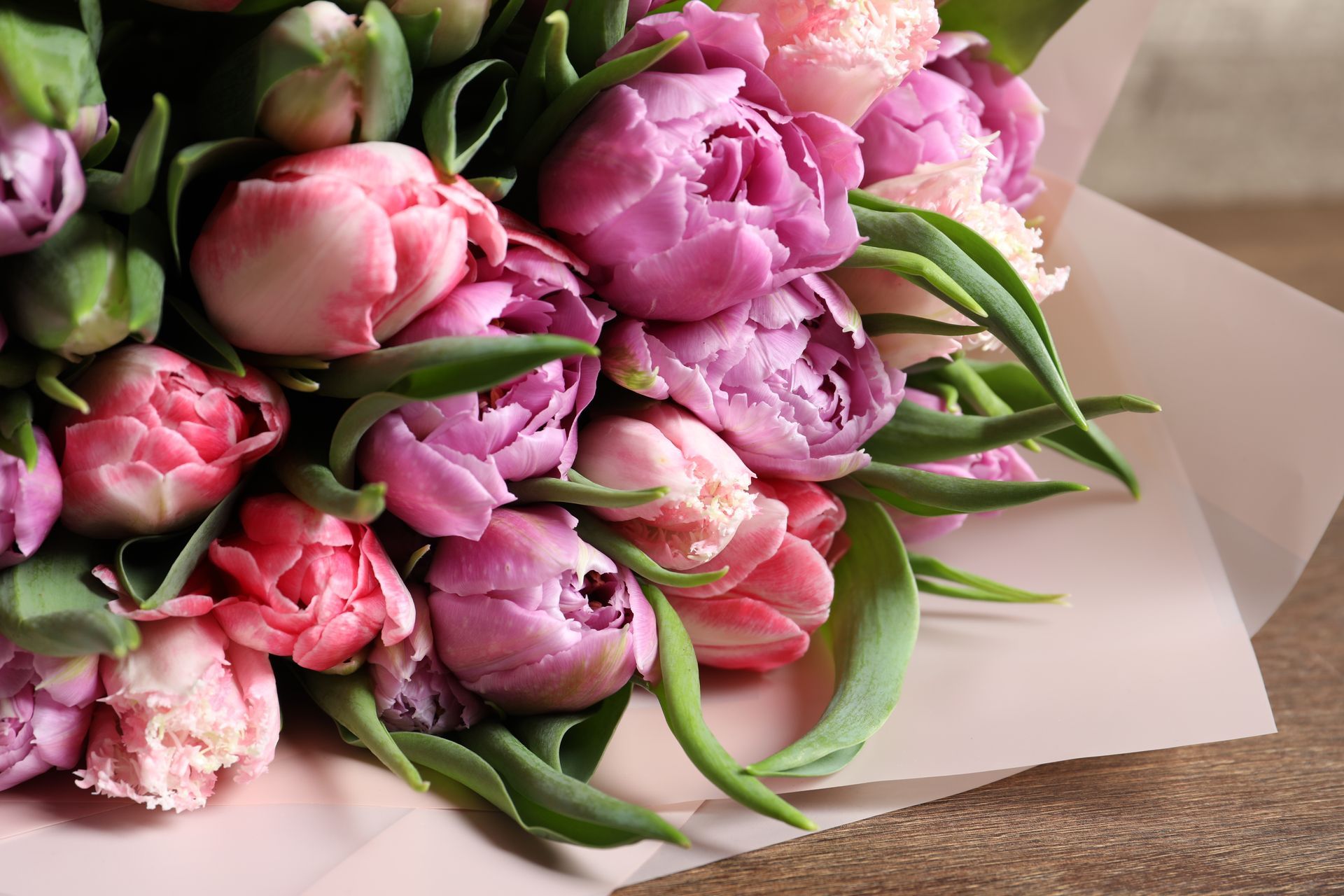 Pink and purple tulip bouquet wrapped in white paper on a wooden table