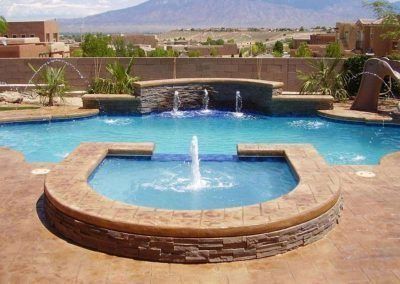 Swimming pool with fountain, water features, and arid landscape backdrop.