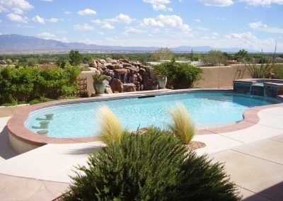 Swimming pool with waterfall feature overlooking a vast landscape under a blue sky.