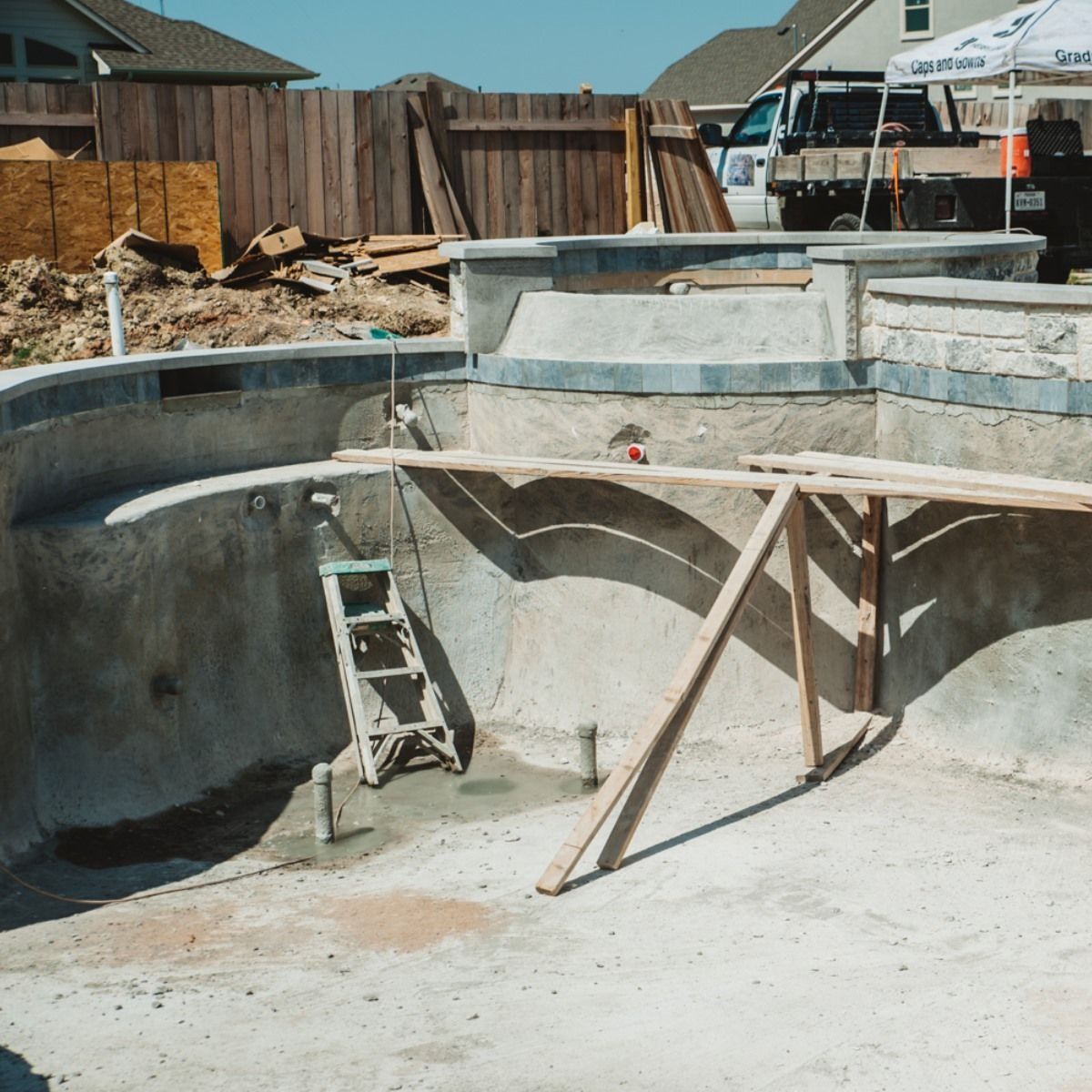 Pool under construction with a wooden support structure.  A ladder is inside, near a partially built wall.