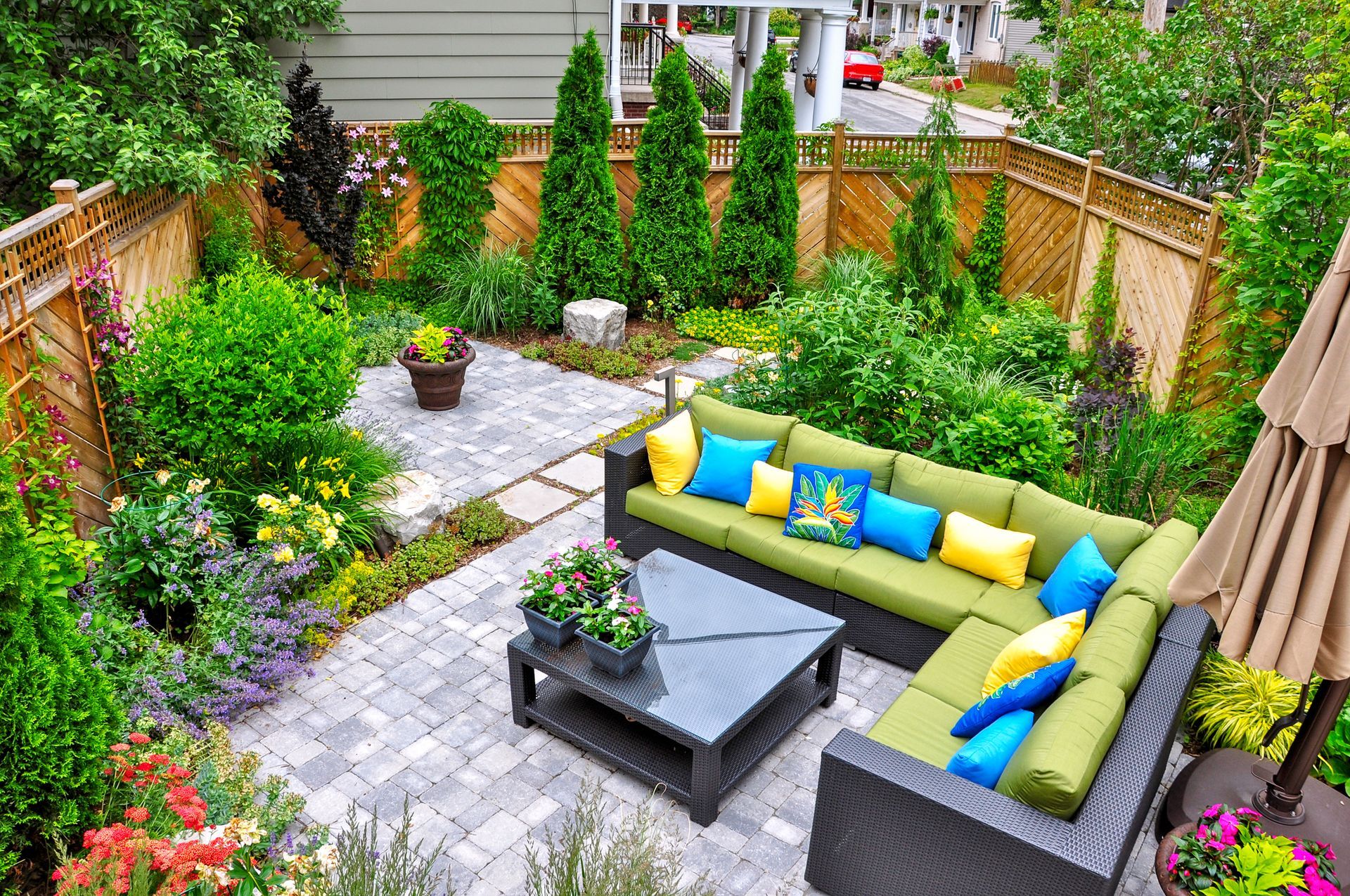 A patio with a couch , table , and umbrella in a garden.