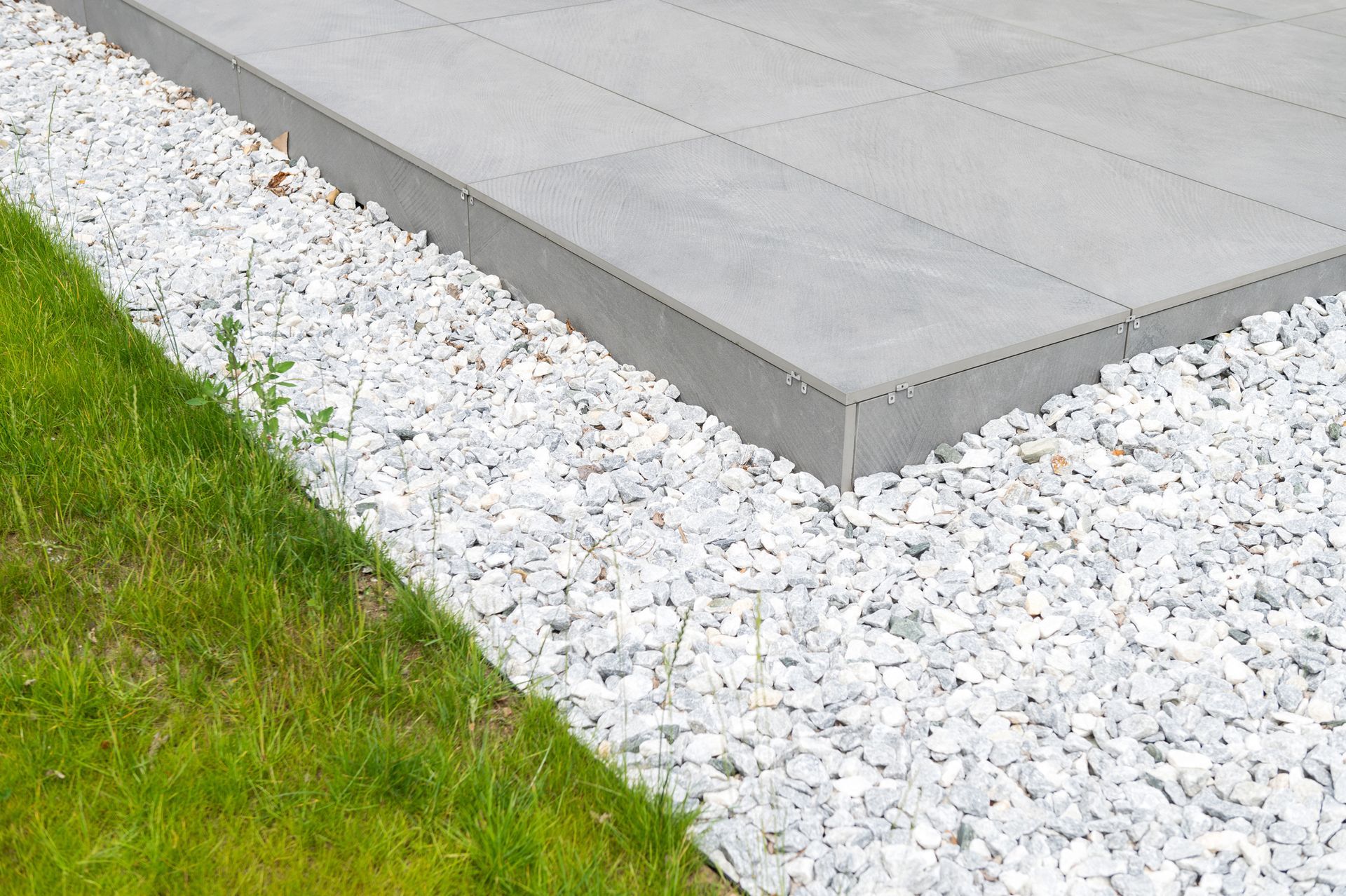 A patio with white gravel and grass on the side of it.