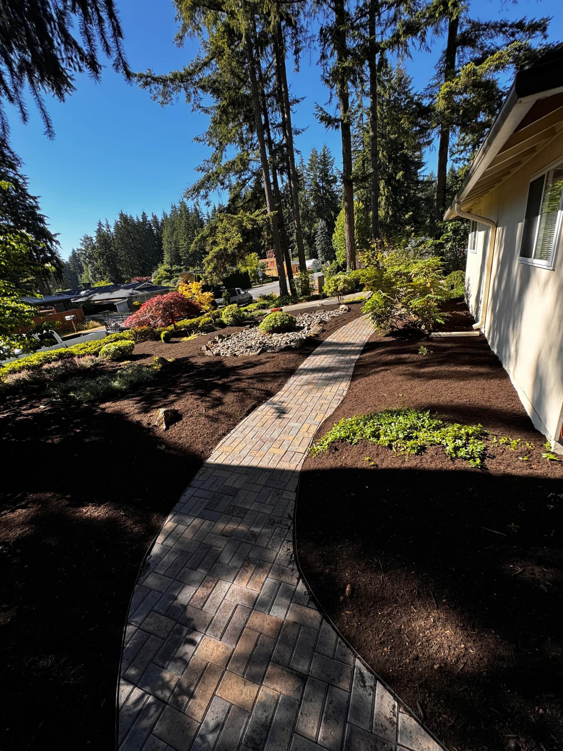 A brick walkway leading to a house surrounded by trees