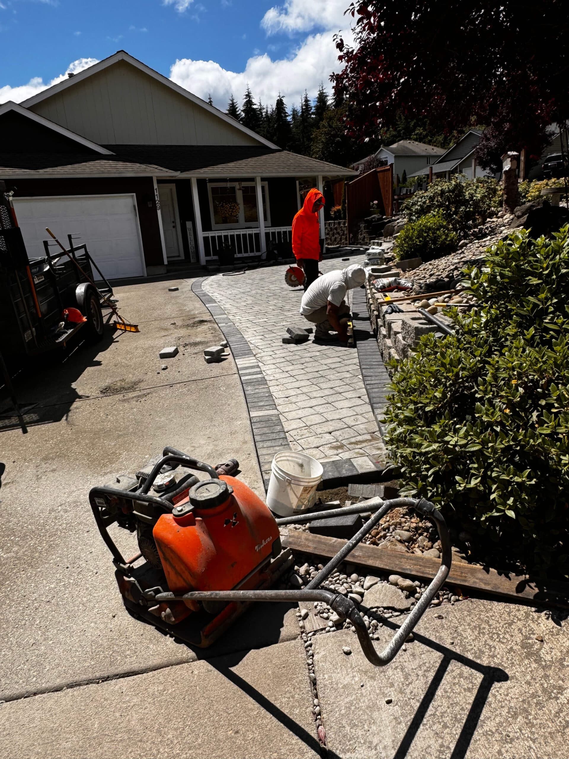 A man is working on a driveway in front of a house.