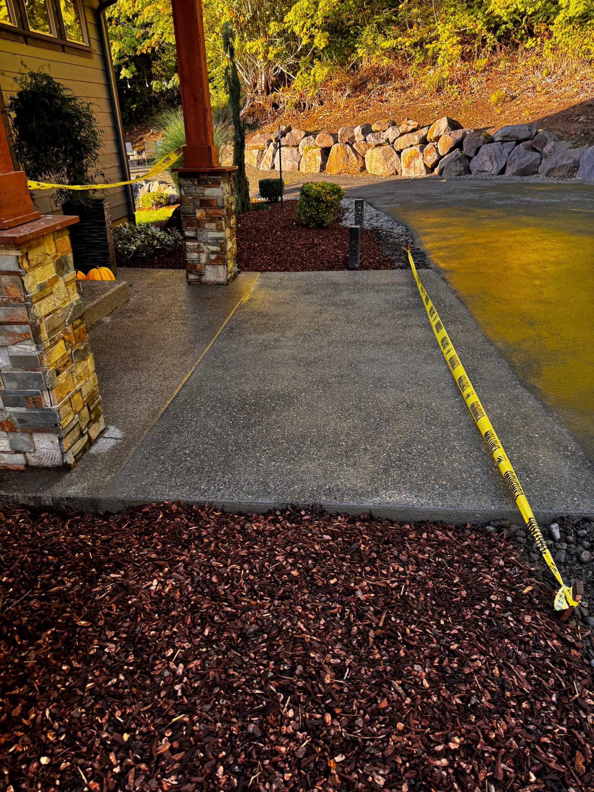 A yellow tape measure is laying on the ground next to a concrete walkway.