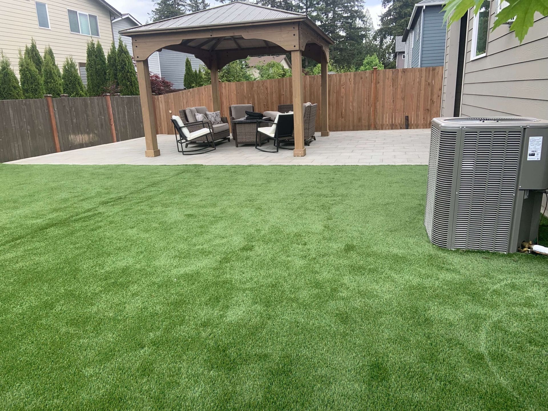 A backyard with a gazebo , patio , chairs and a air conditioner.