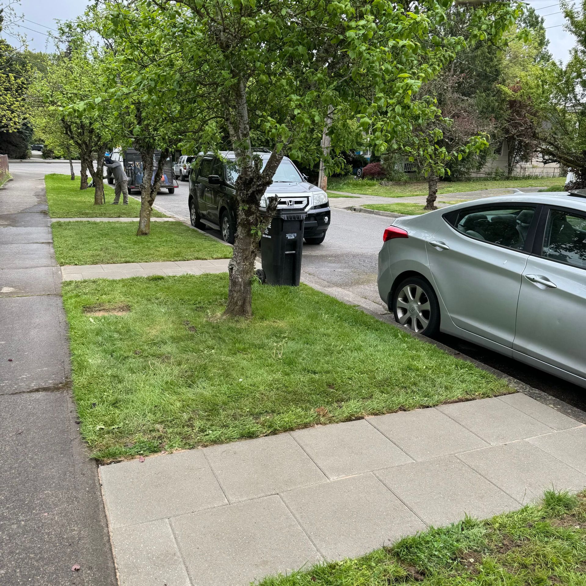 A silver car is parked on the side of the road next to a sidewalk.