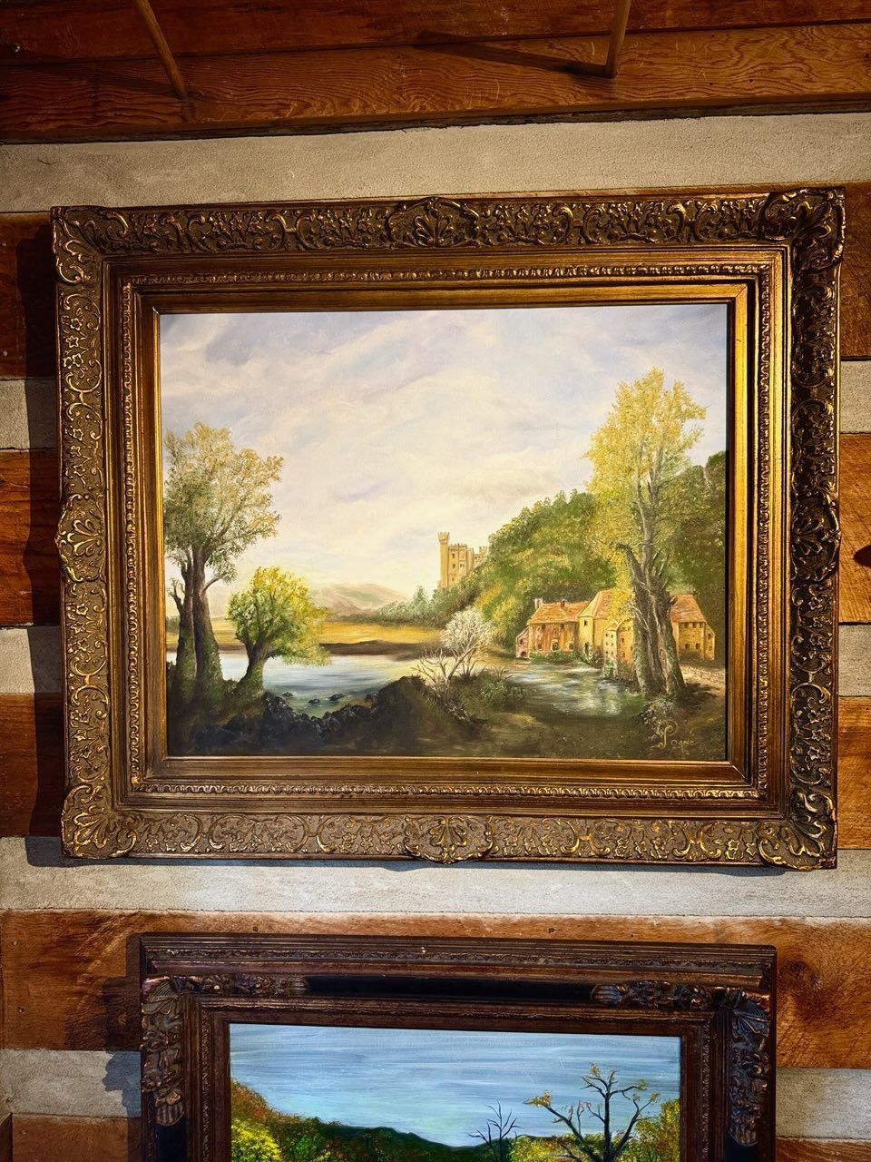 A painting in a gold frame is hanging on a wooden wall