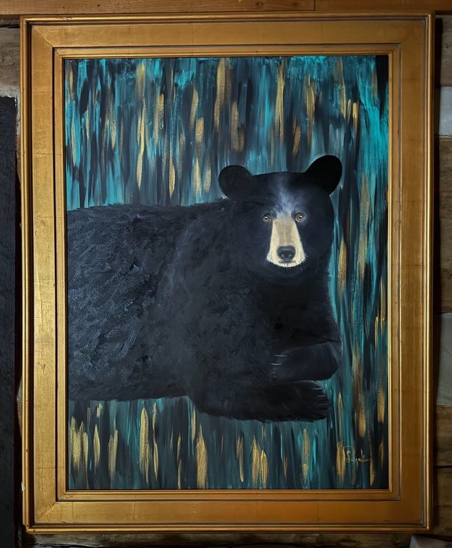 A black bear is laying down in a painting in a gold frame.