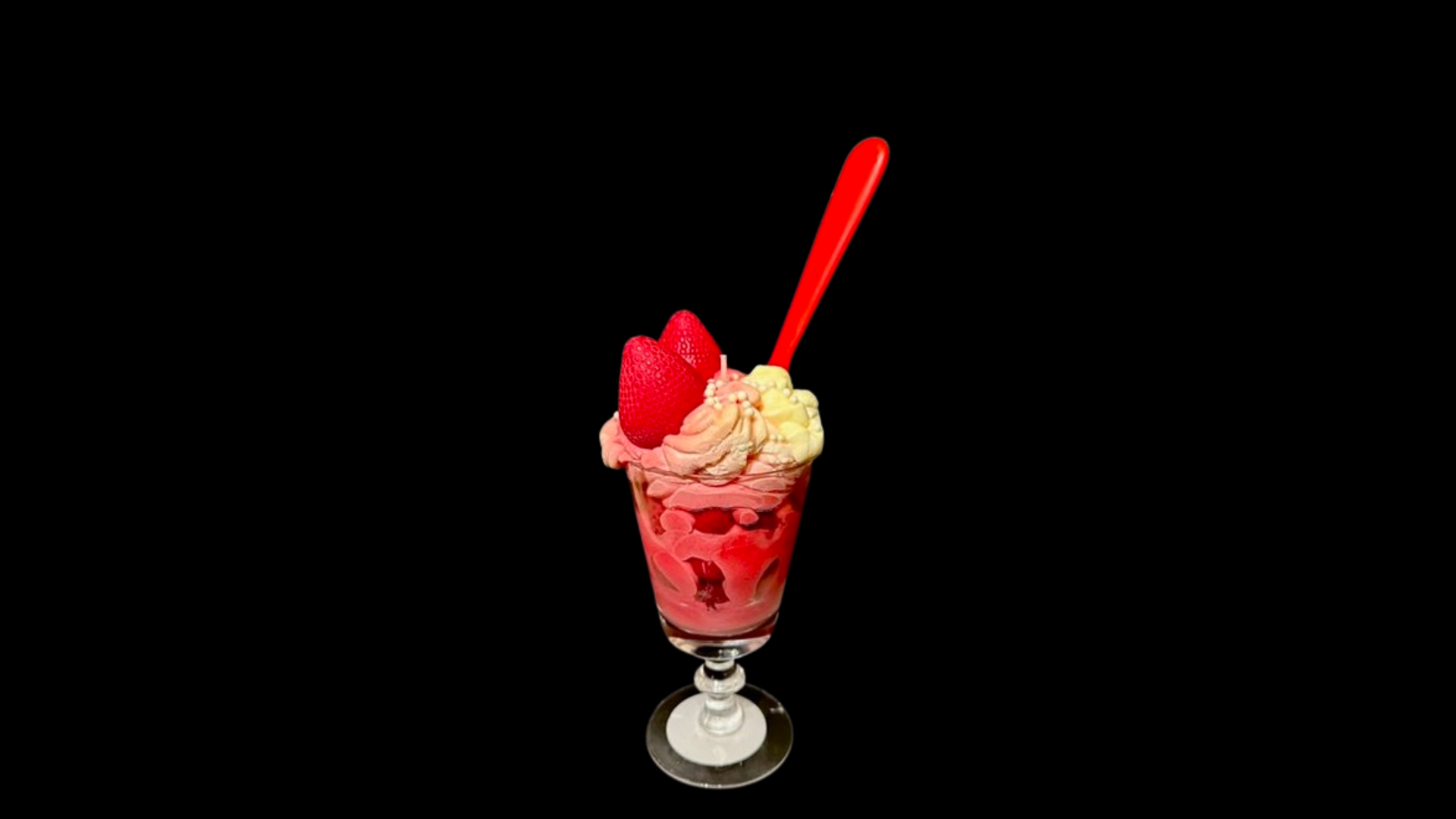 A glass of ice cream with a spoon in it on a black background.