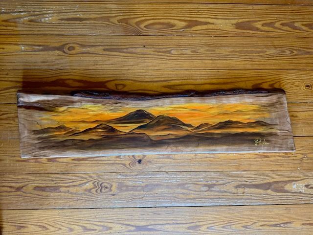 A painting of a mountain range is sitting on a wooden floor.