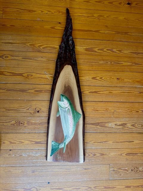 A fish is carved into a piece of wood on a wooden floor.