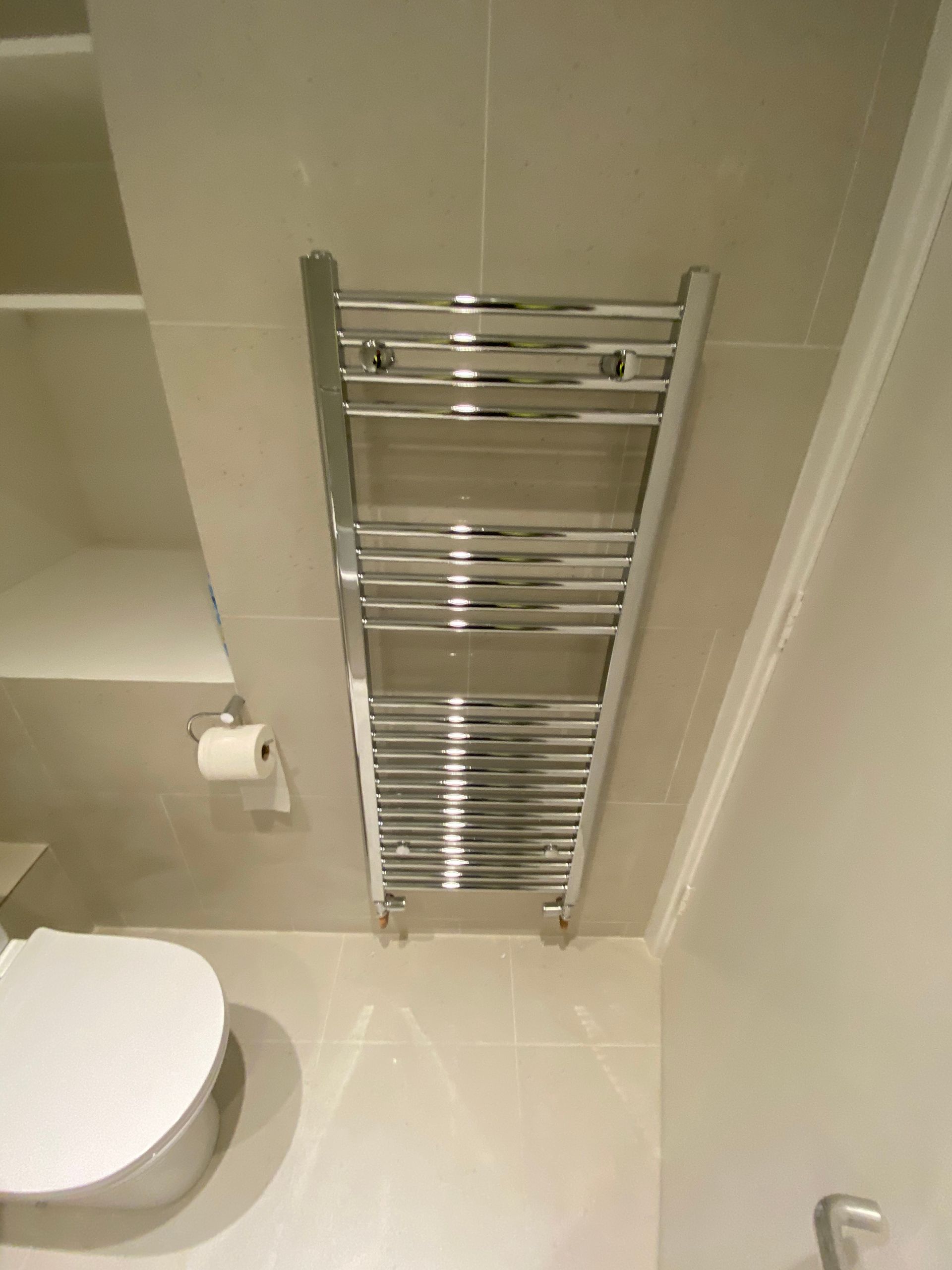 Chrome heated towel rail on modern wall tiles in a renovated Hackney E5 bathroom conversion.