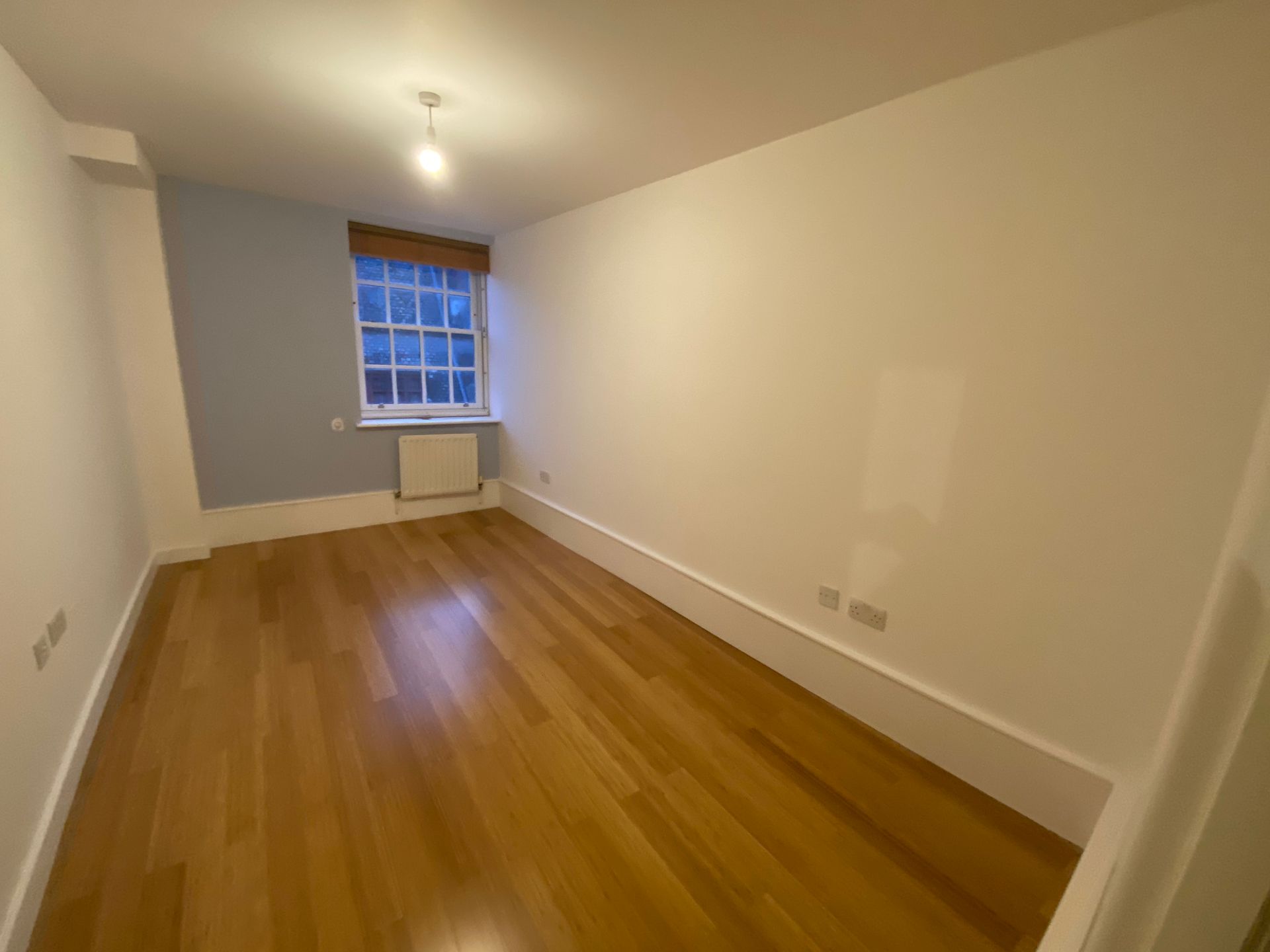 Newly renovated bedroom with light blue accent wall and hardwood floors in a Hackney E5 flat conversion.