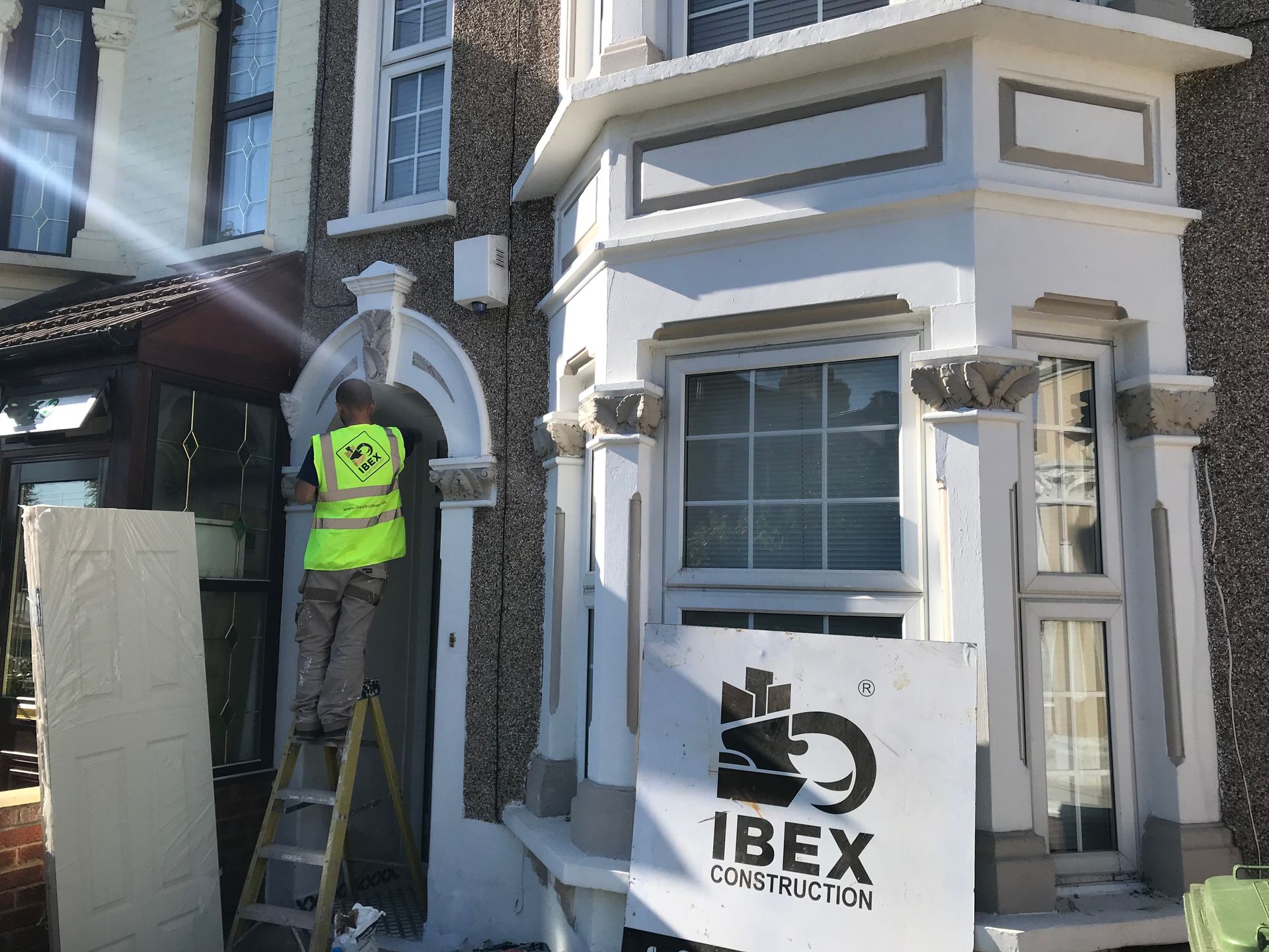 IBEX builder in a high-visibility vest performing exterior maintenance on a white Victorian house.