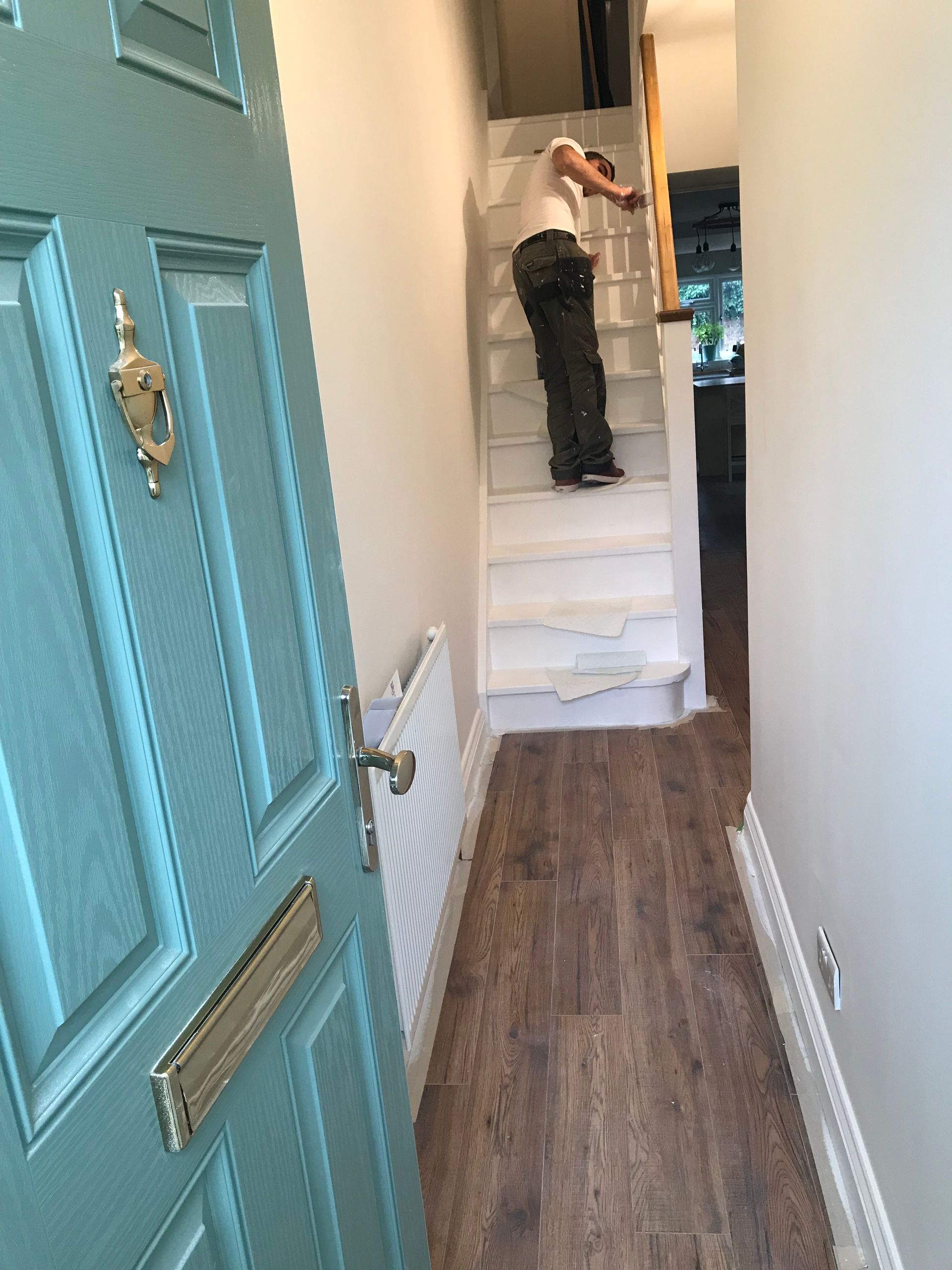 Contractor installing wooden banister on white stairs, viewed through an open teal front door.