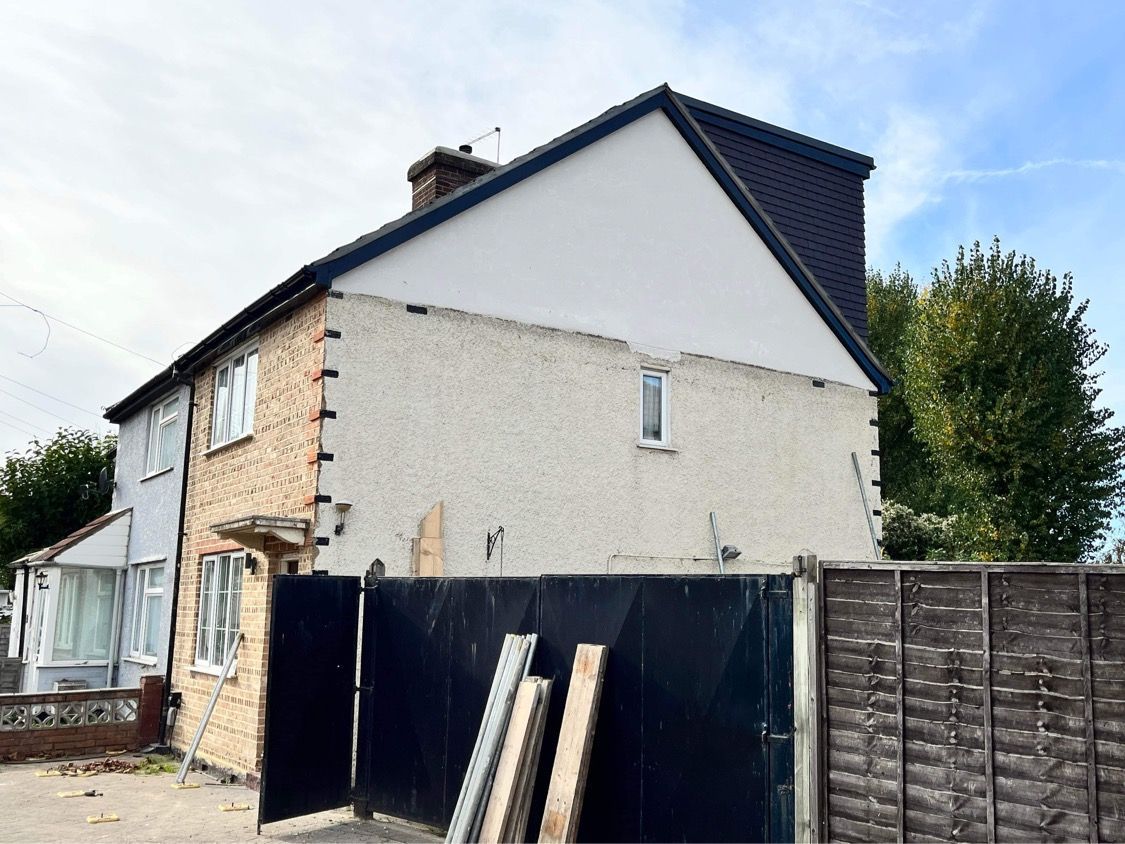 Side profile of a residential house showing a newly completed black dormer loft conversion against the sky.