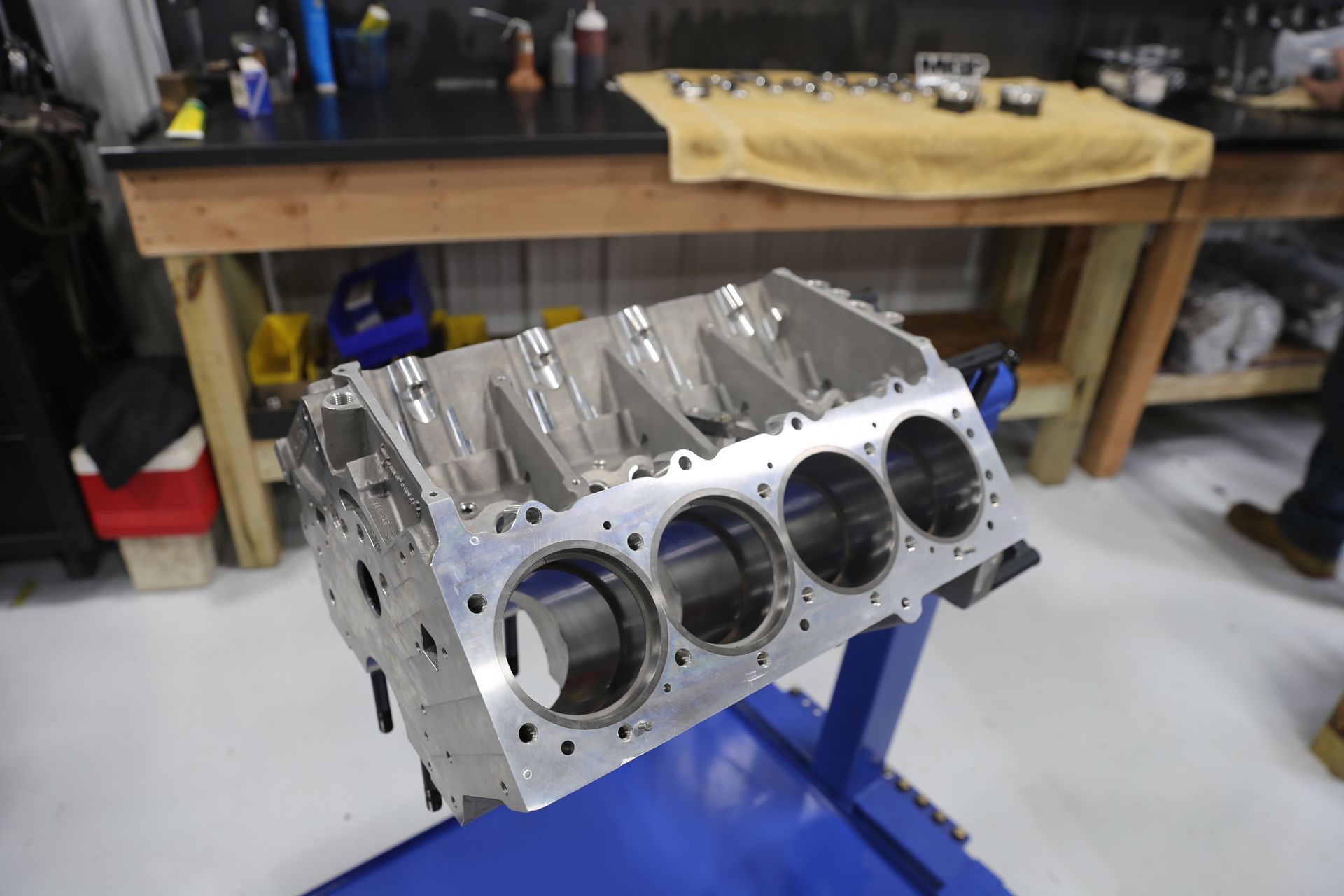 Engine block, metallic silver, mounted on a blue stand, in a workshop setting.