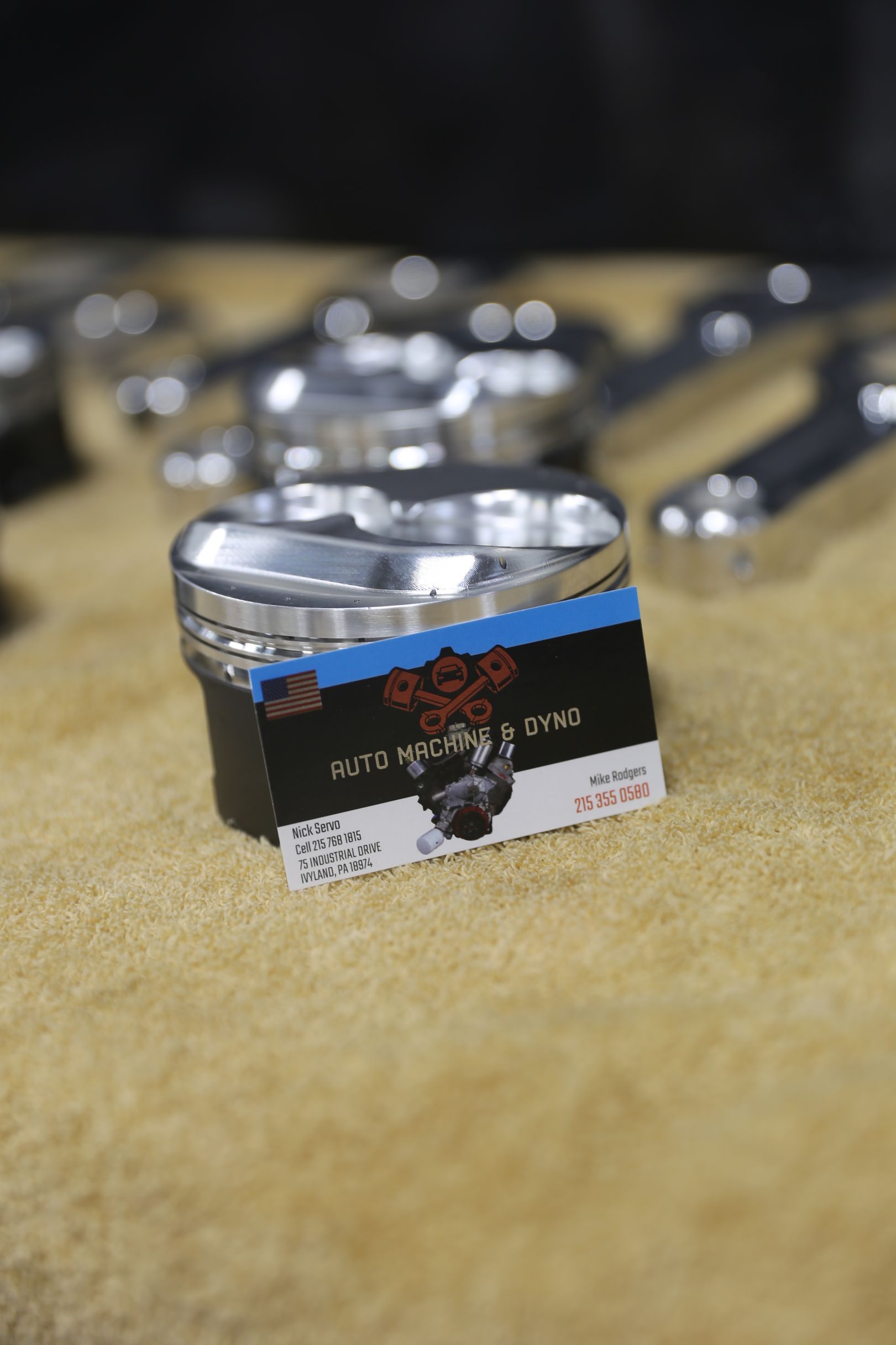 A metallic grinder with a business card on a tan surface, surrounded by other metallic objects.