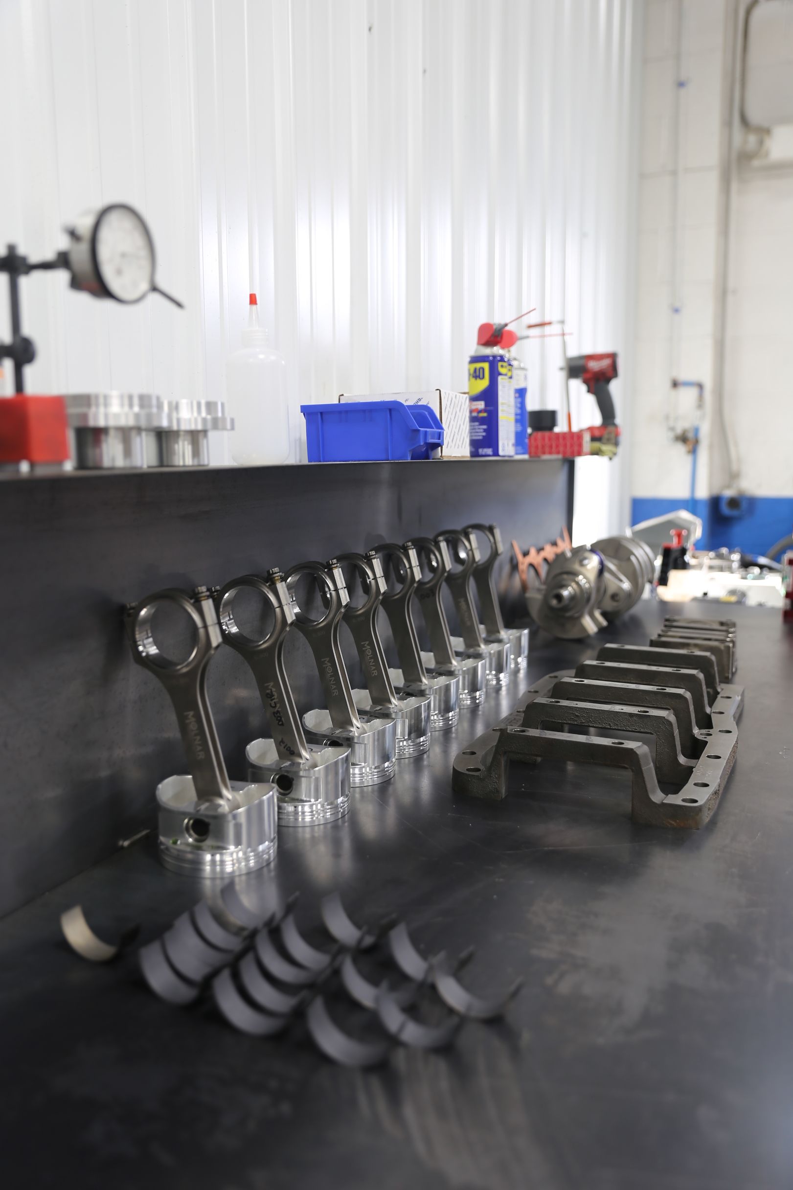 Engine parts laid out on a table in a workshop, including pistons, connecting rods, and a crankcase.