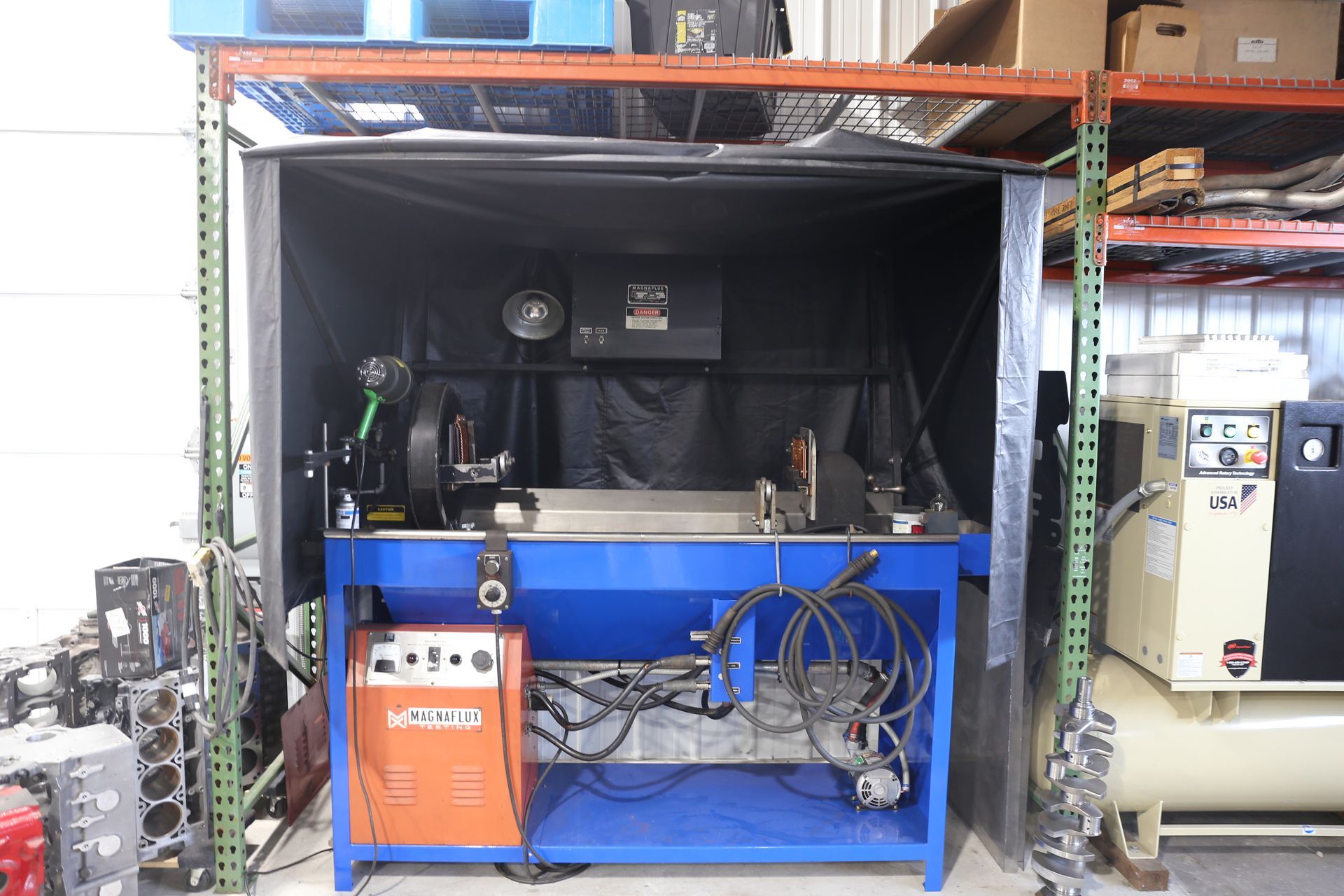 Welding station: blue table with welding equipment inside a black-curtained enclosure, in a workshop.