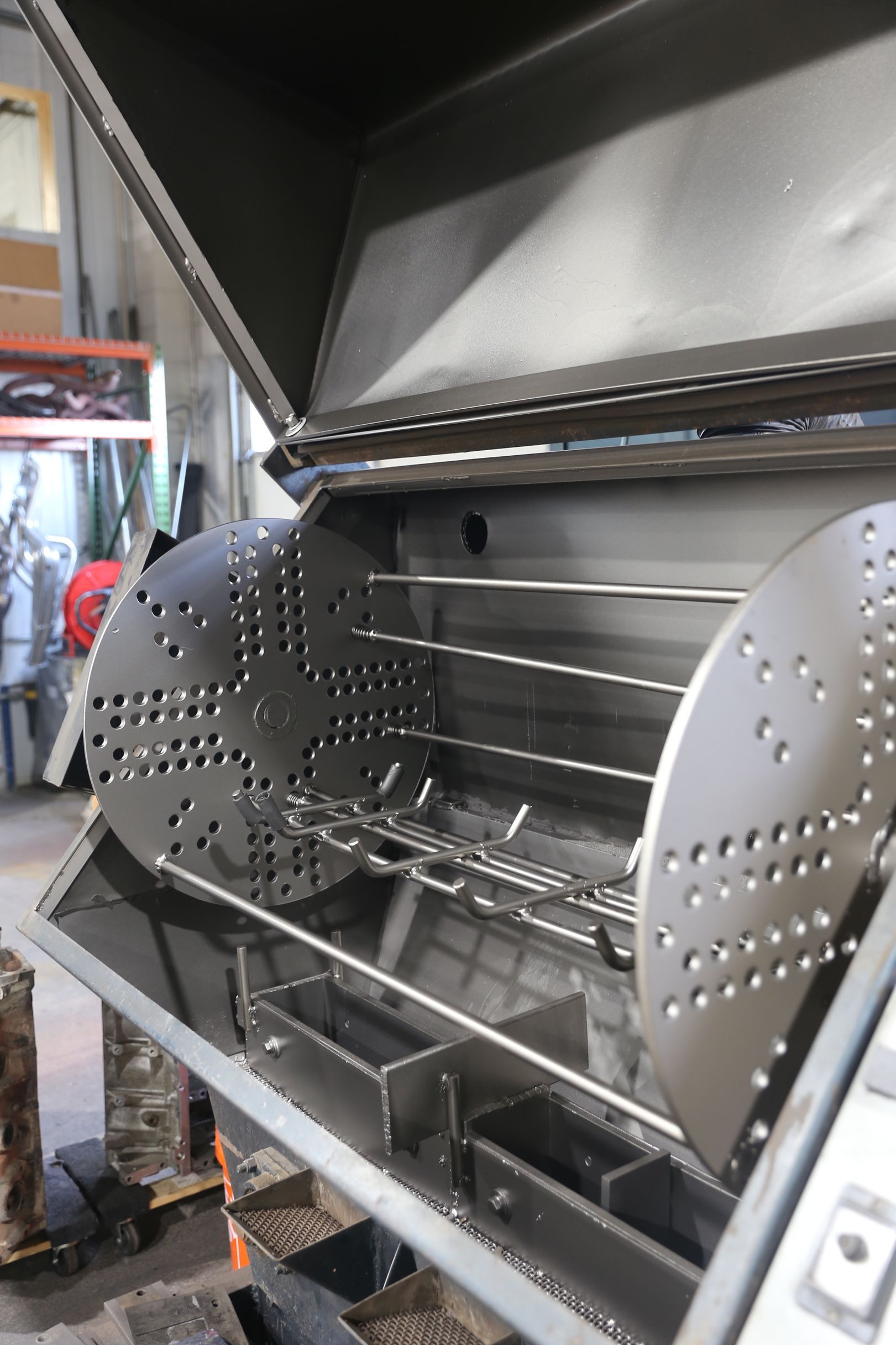 Stainless steel rotisserie grill with open lid, interior with racks, and perforated side panels.