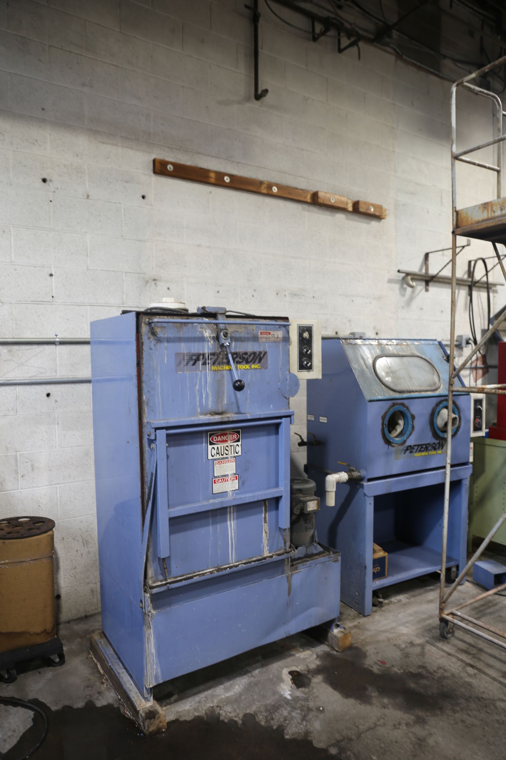 Blue industrial machines, possibly for metalwork, against a white wall in a workshop.