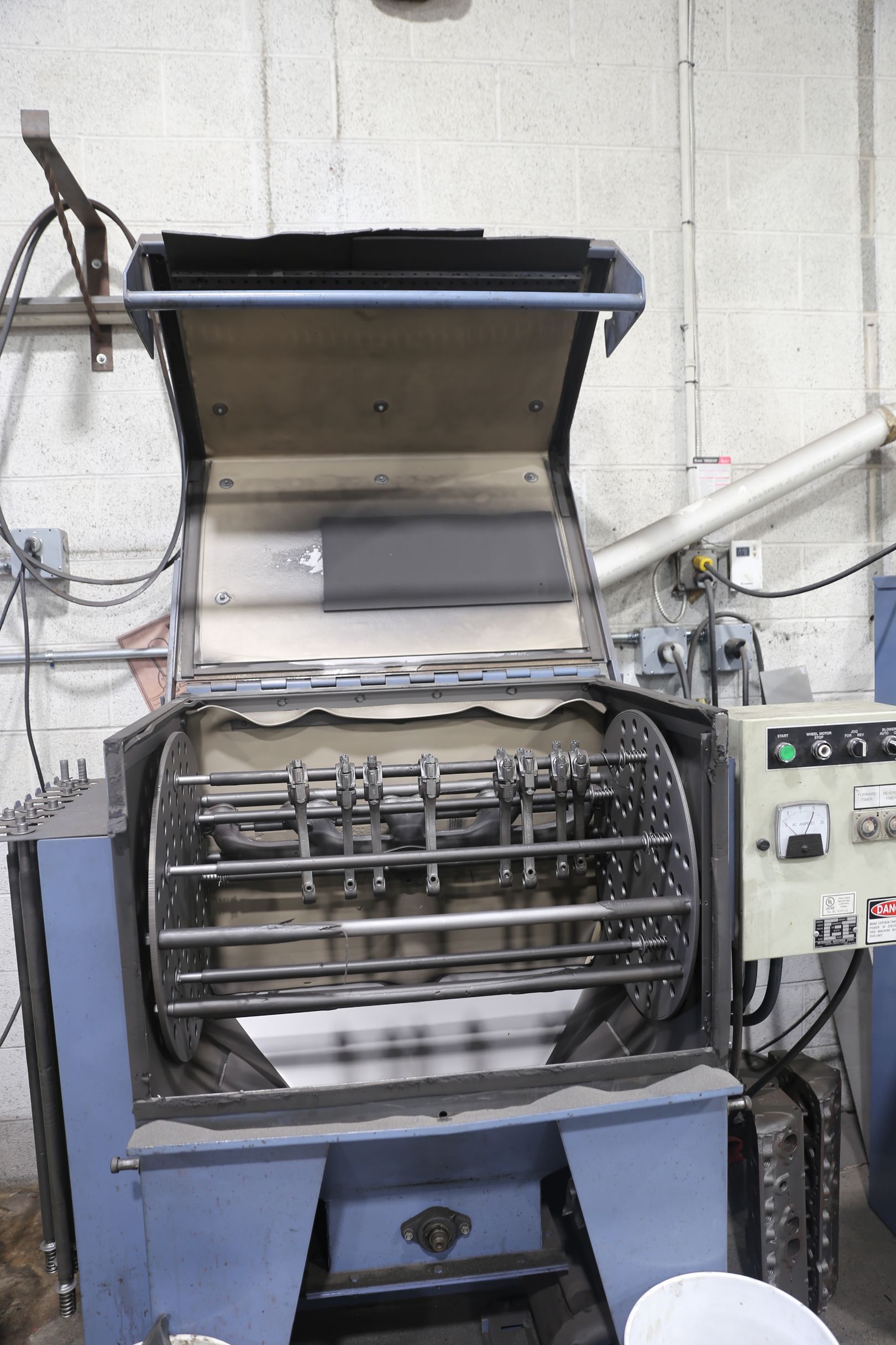 Blue industrial tumbler machine with open lid and rotating metal bars inside.