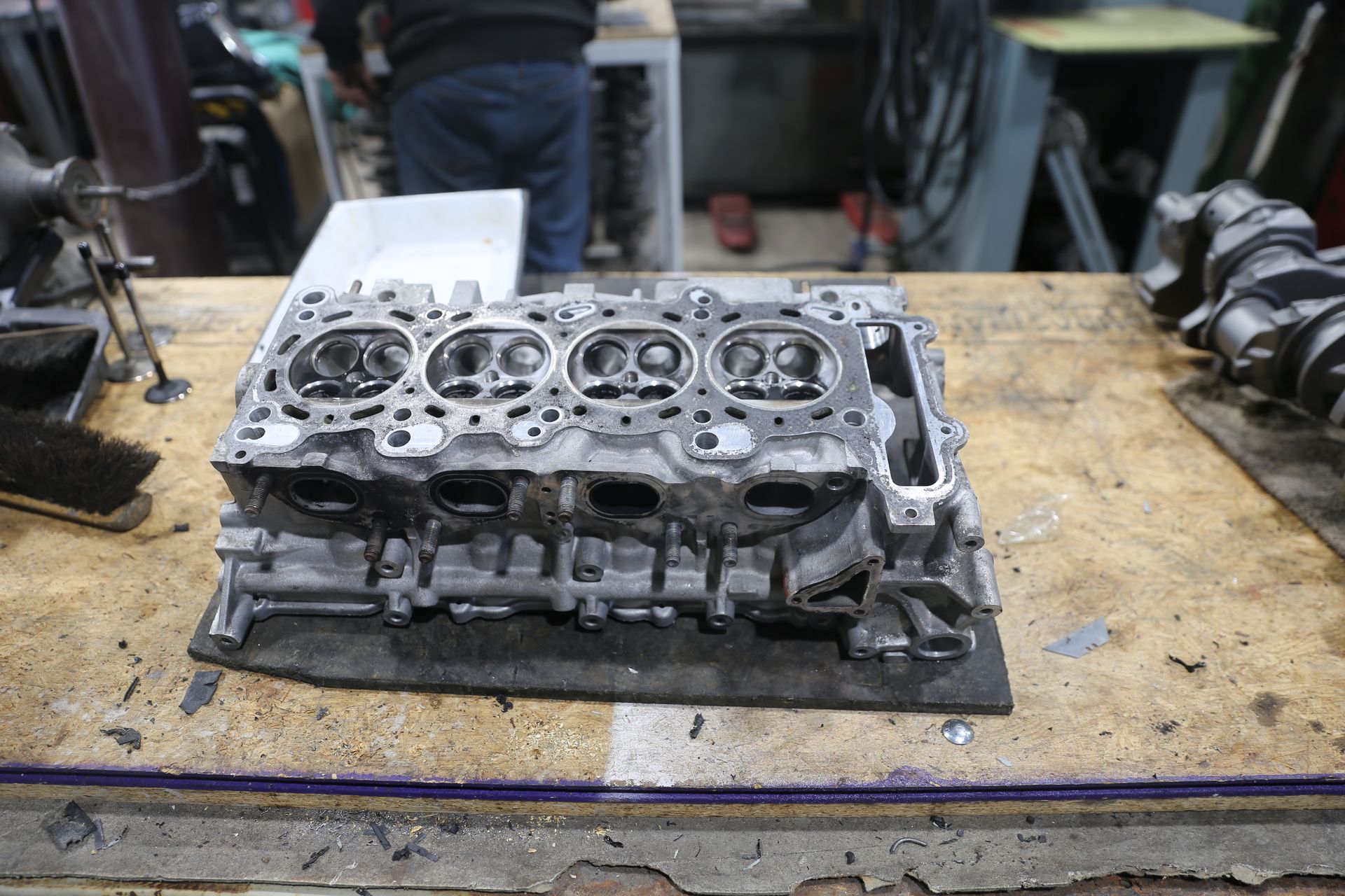 Engine cylinder head on a workbench; person in background.
