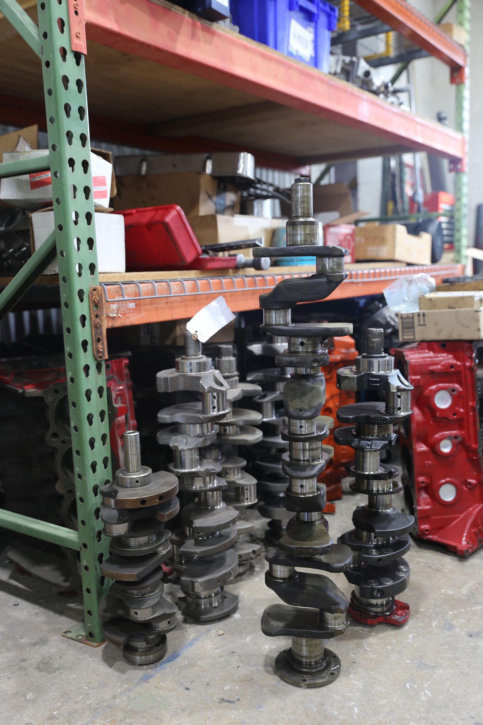 Several crankshafts standing in front of shelves filled with automotive parts.