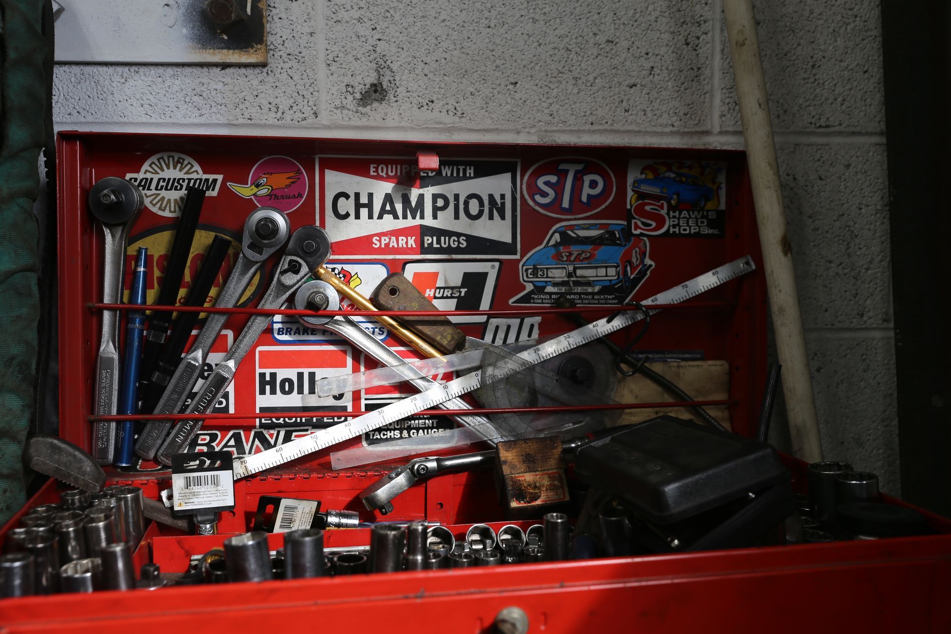 Red toolbox filled with tools, sporting racing decals, in a garage setting.
