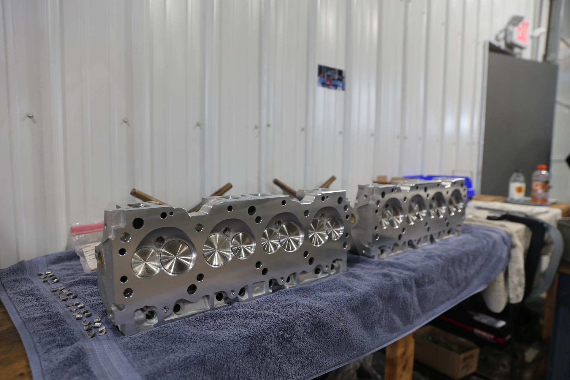 Two polished engine cylinder heads on a blue towel in a workshop.