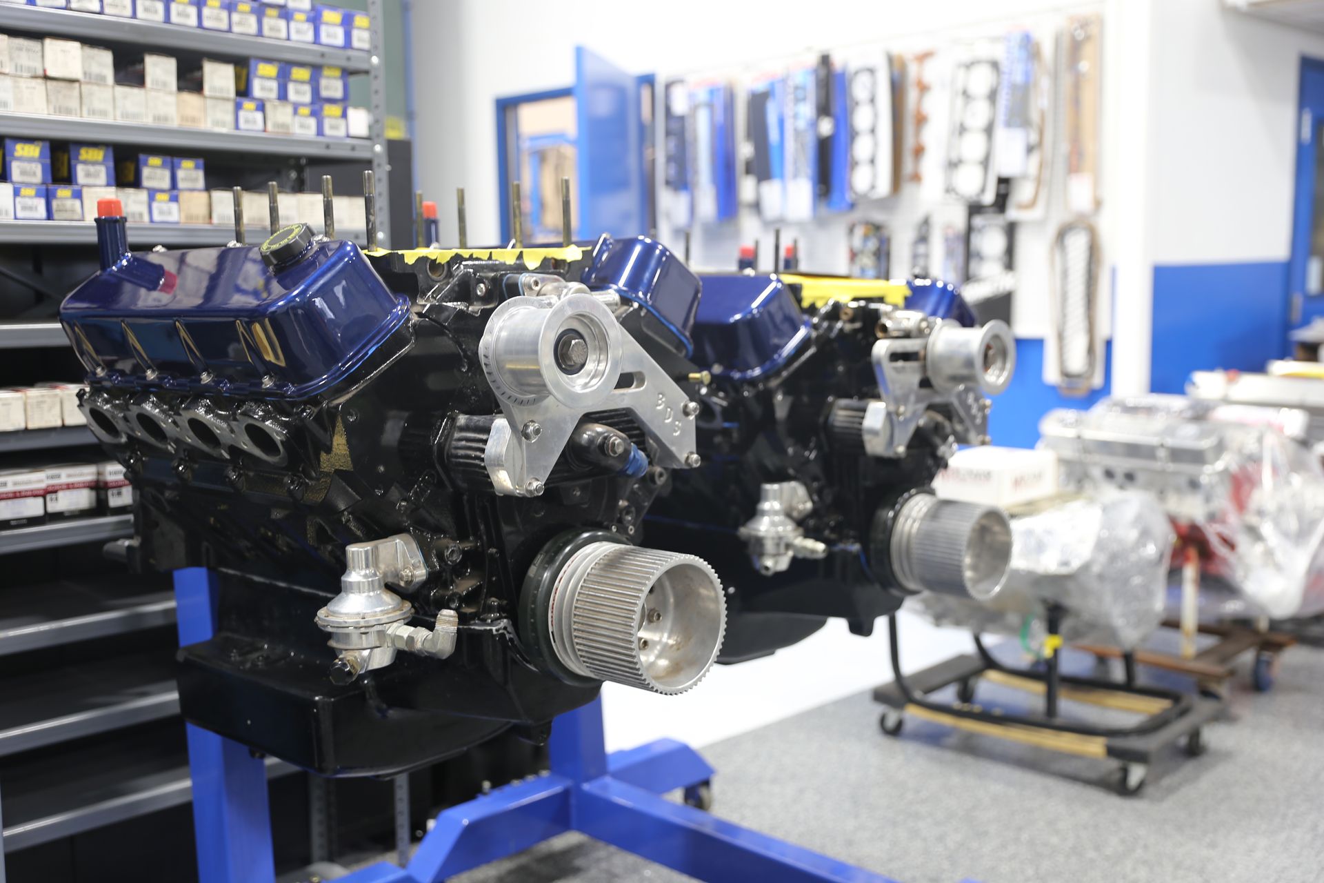 Blue and black engine on a blue stand in a shop, parts on shelves and walls.