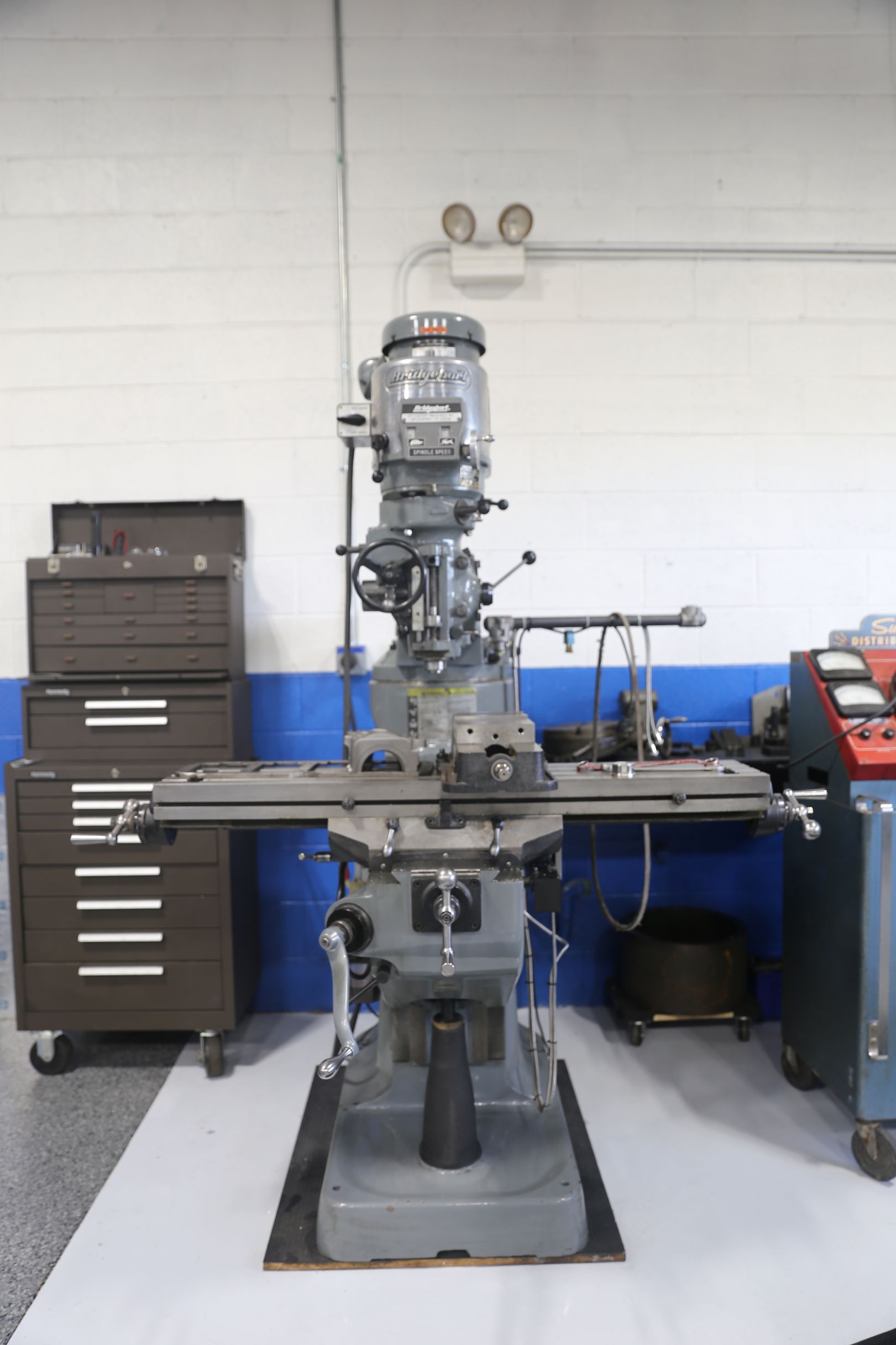 A large gray milling machine in a workshop with tool cabinets and a blue wall.