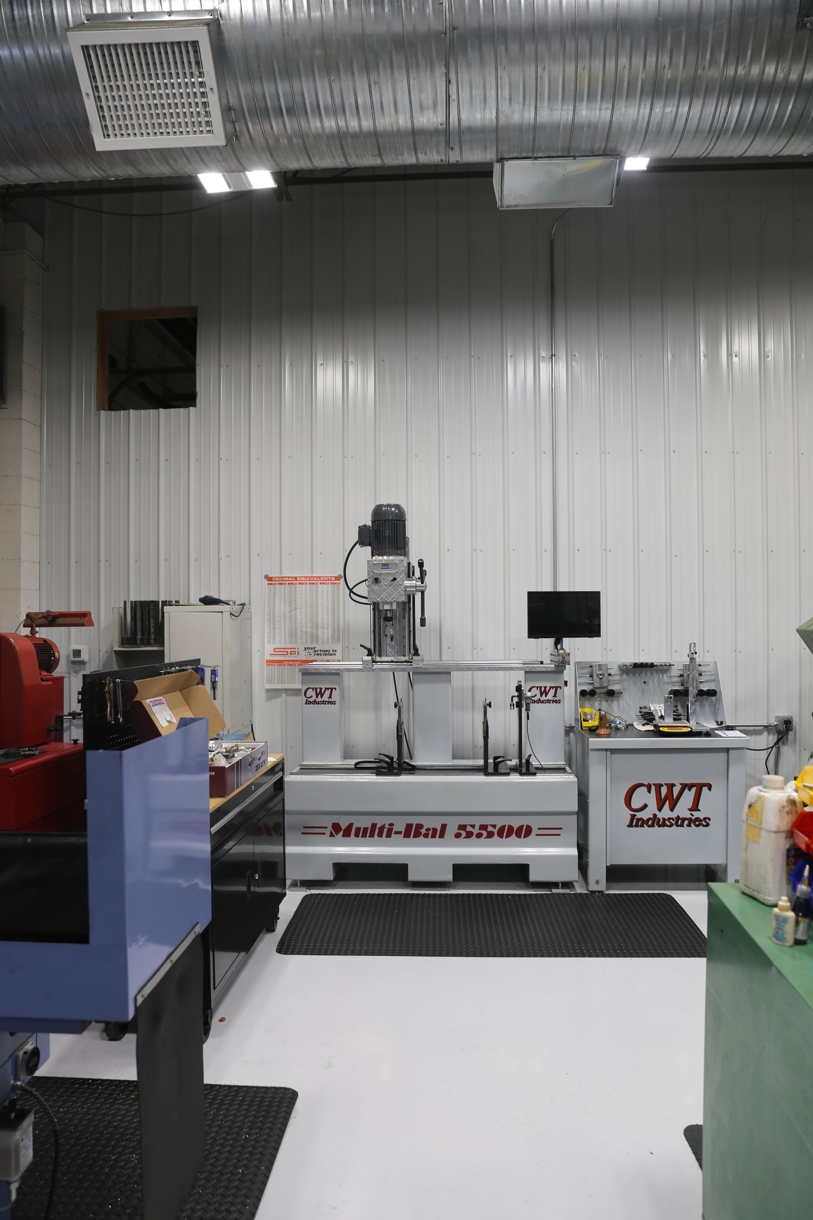 Workshop interior with machinery: balancing machine, mill, and lathe against a white-paneled wall.