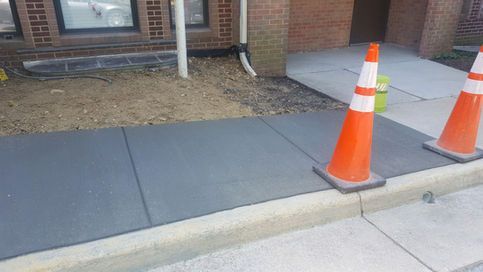 Freshly poured gray sidewalk, two orange cones, and building entrance.