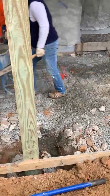 Person installing a wooden post in a hole with rebar, gravel, and tools in construction site.