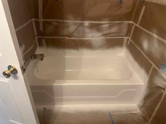 Bathroom renovation with white tub, walls masked in brown paper, and white paint spray.