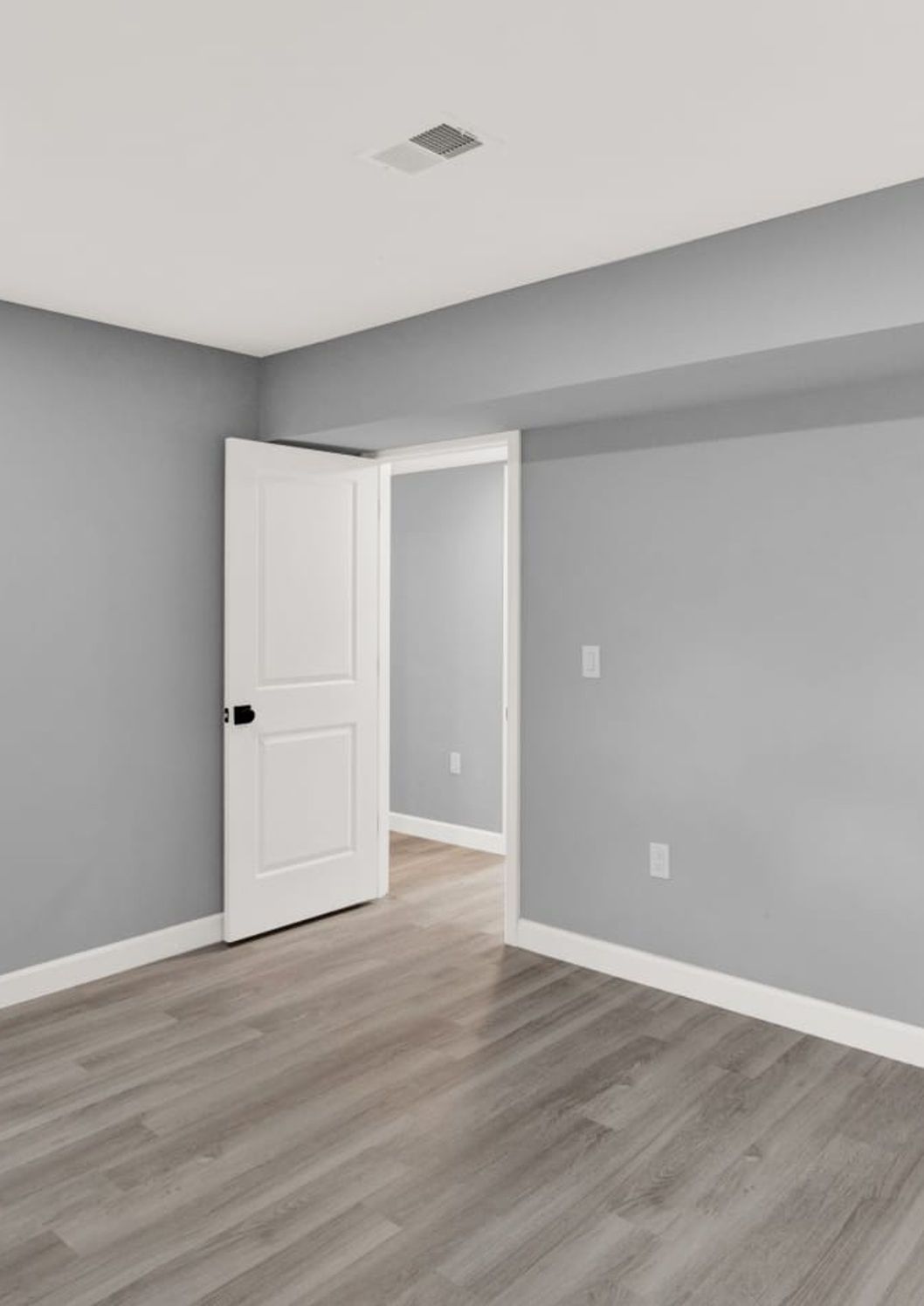 Empty room with gray walls, white trim, and open door, with light-colored wood flooring.