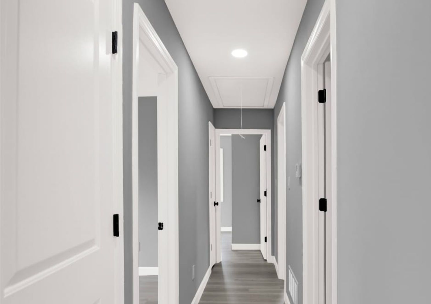 Long hallway with white doors, grey walls, and a light on the ceiling.
