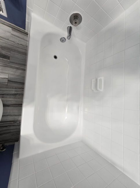 White bathtub with showerhead, soap dish, and tiled walls.