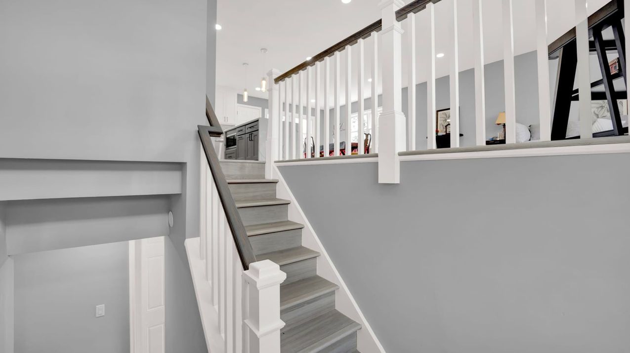Gray staircase with white railing leading up to a landing overlooking a brightly lit room.