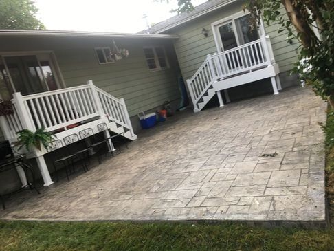 Concrete patio with stamped pattern next to a house with white decks and green siding.