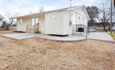 Tan house with a concrete patio, a wooden deck, and a dry, brown lawn.