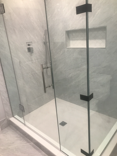 Glass shower enclosure with white marble-like walls, chrome fixtures, and black door hardware.