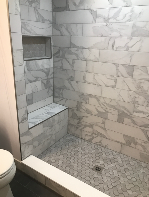 Marble-tiled shower with built-in bench and niche. Hexagonal tile floor. Toilet visible on the left.